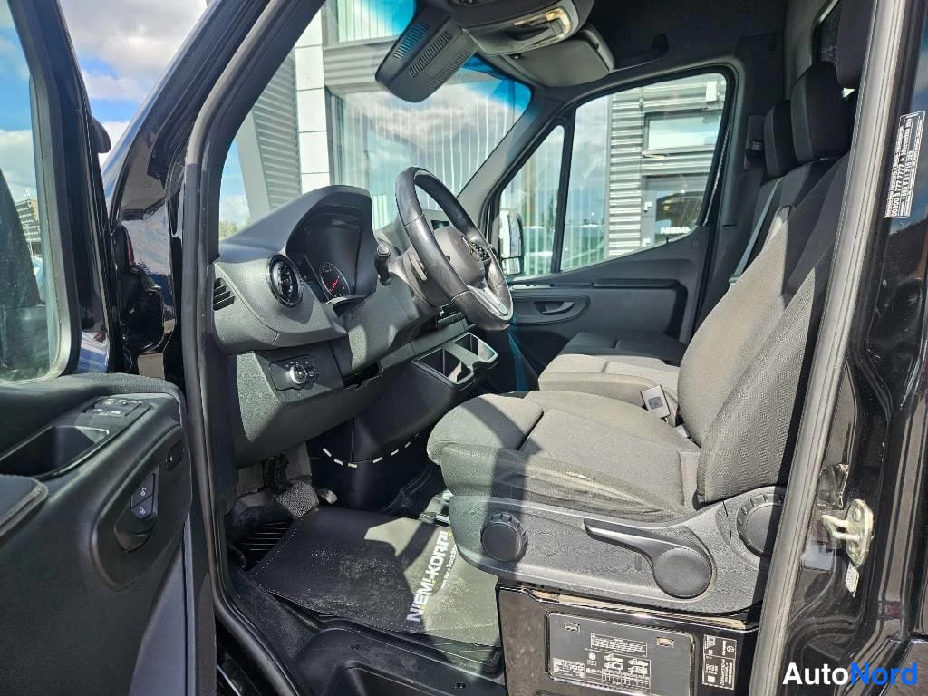 Ohjaamo: View into the cab through the open driver's door, showing the driver's seat, dashboard, and steering wheel. A black floor mat with white text is placed over the
