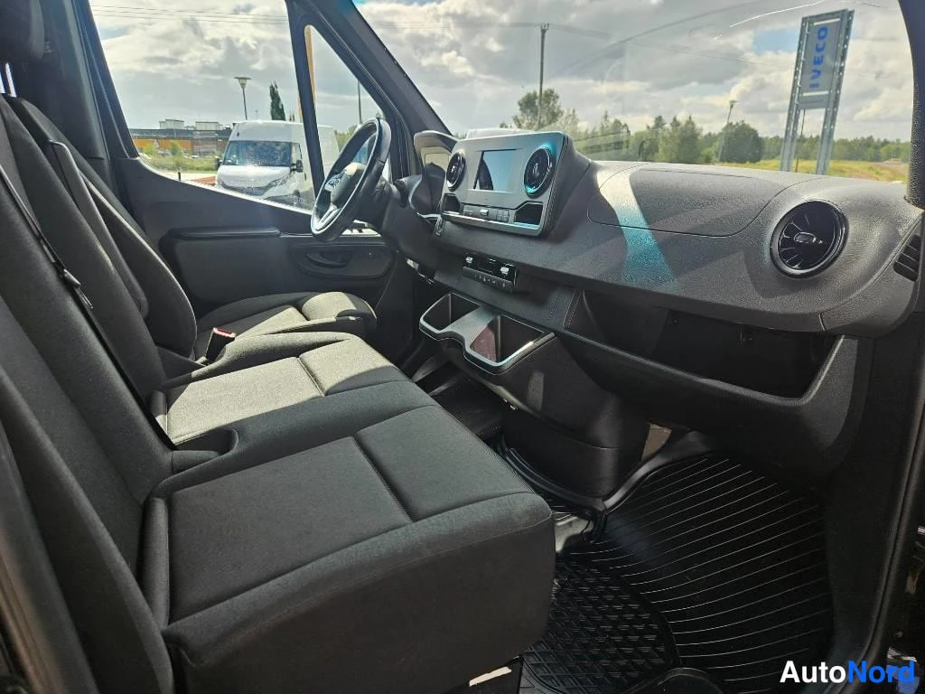 Ohjaamo: Wide interior shot showing the front bench seats and dashboard. Through the windshield, an IVECO dealership sign is visible in the background. The car appears t