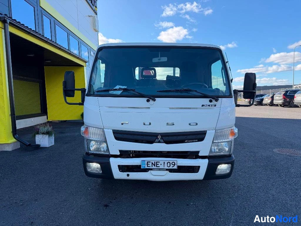 Edestä: Valkoisen Mitsubishi Fuso Canter -kuorma-auton etupää suoraan edestä, rekisterikilpi ja FUSO-teksti konepellissä.