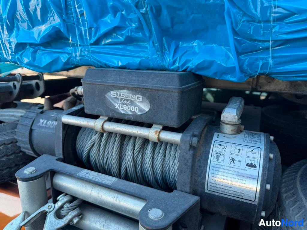 Yksityiskohta: Close-up of a winch labeled Strongline XL9000 under blue plastic sheeting.