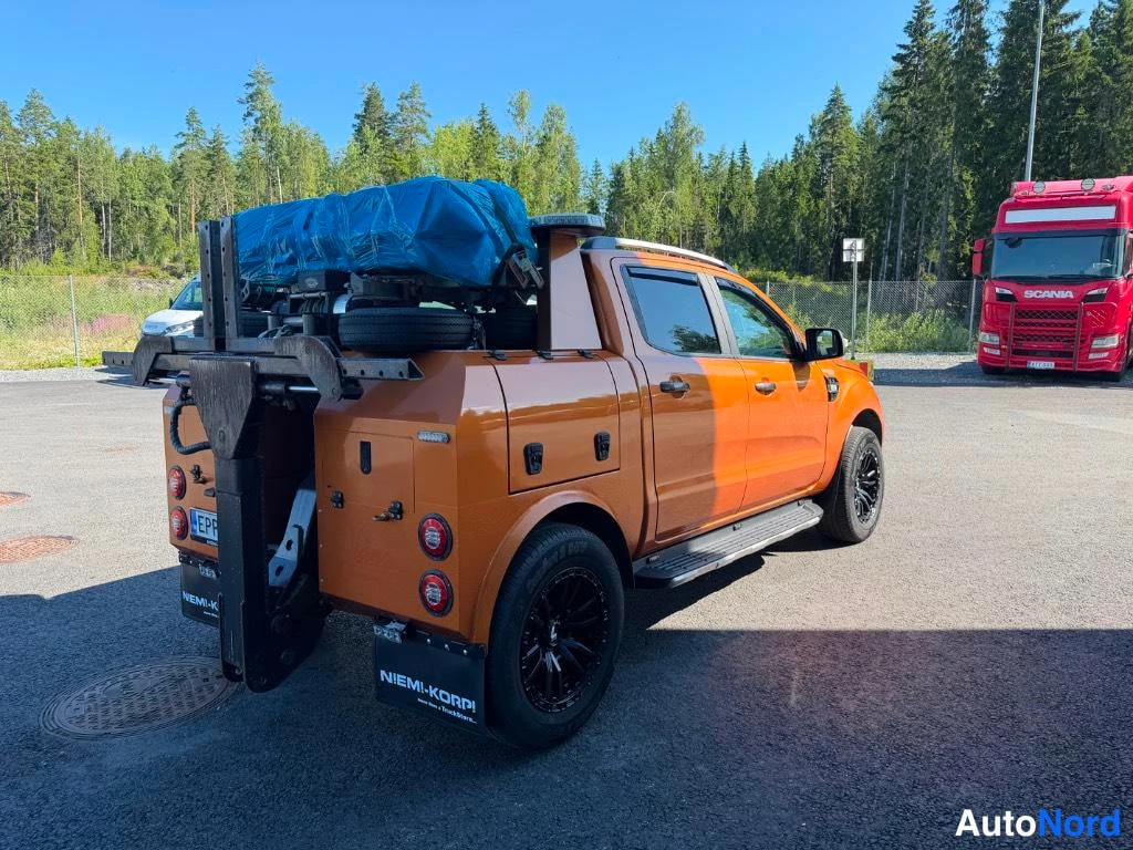 Takaviisto: Oranssi avolava-auto takaviistosta vasemmalta; lavalla sininen kuorma ja mustat pyörät.