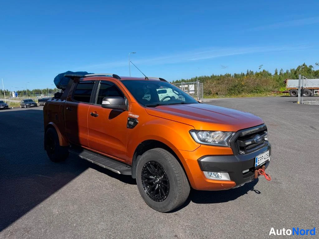 Etuviisto, nokka oikealle: Oranssi avolava-auto edestä oikealta; mustat vanteet ja sivuoven pieni kuva.
