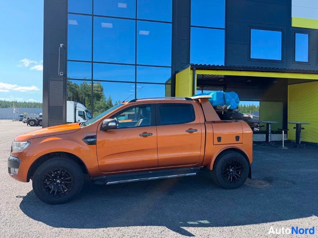 Sivulta: Orange four-door pickup truck parked outside a glass building.