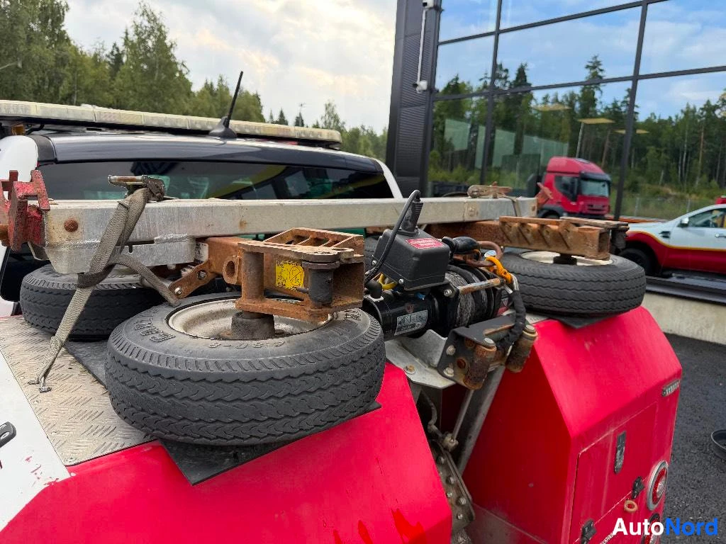Yksityiskohta: Lähikuva auton takaosaan liittyvistä laitteista. Näkyy kolme rengasta, joita pidetään paikallaan kiinnikkeillä, sekä musta moottori ja kaapeli. Taustalla lasipi