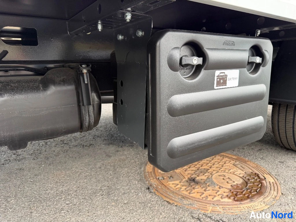 Yksityiskohta: Yksityiskohta alustasta: harmaa koteloin suojakotelo BATTERY-merkinnällä, renkaan ja pakosysteemin osia.