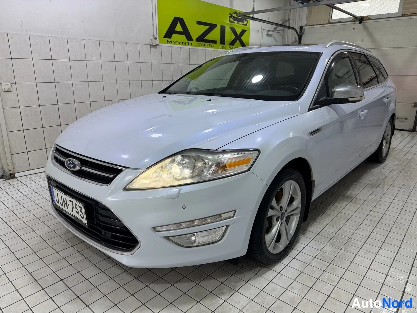 Etuviisto, nokka vasemmalle: Valkoinen Ford Mondeo -farmari kolmannelta edestä, nokka vasemmalla.