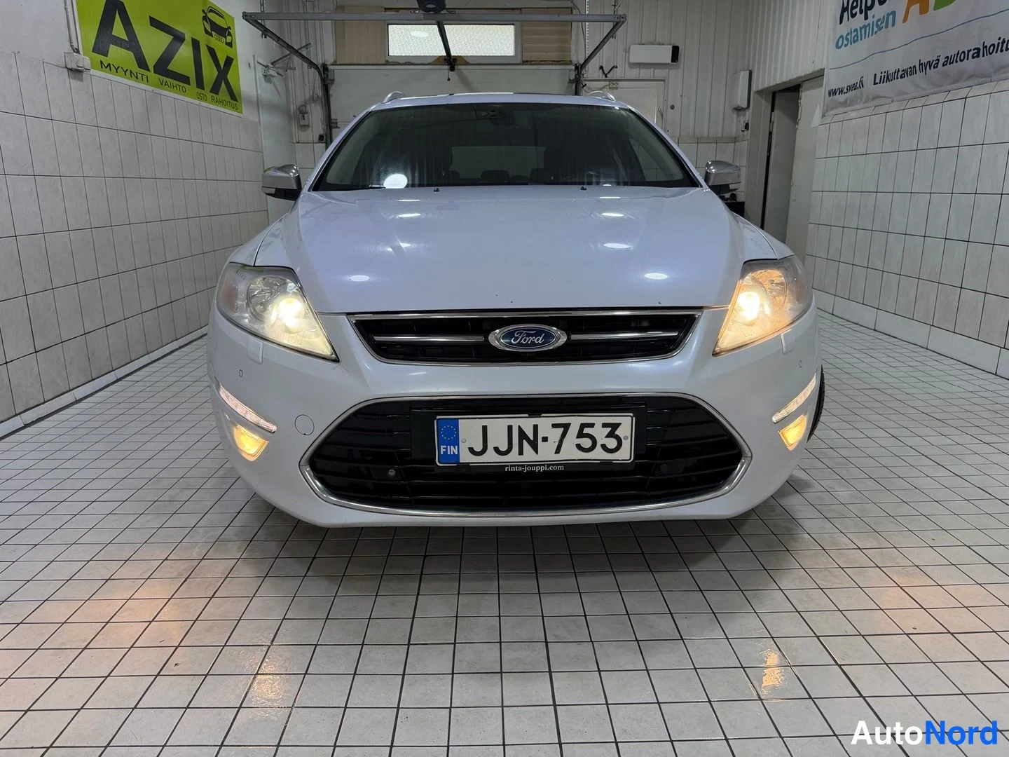 Edestä: Valkoinen Ford Mondeo edestä, sumuvalot päällä, rekisteritunnus.