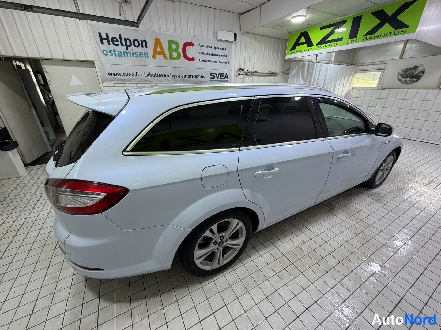 Takaviisto: Valkoisena farmarina kuvattu auto takaa ja oikealta sivulta myyntitilassa.