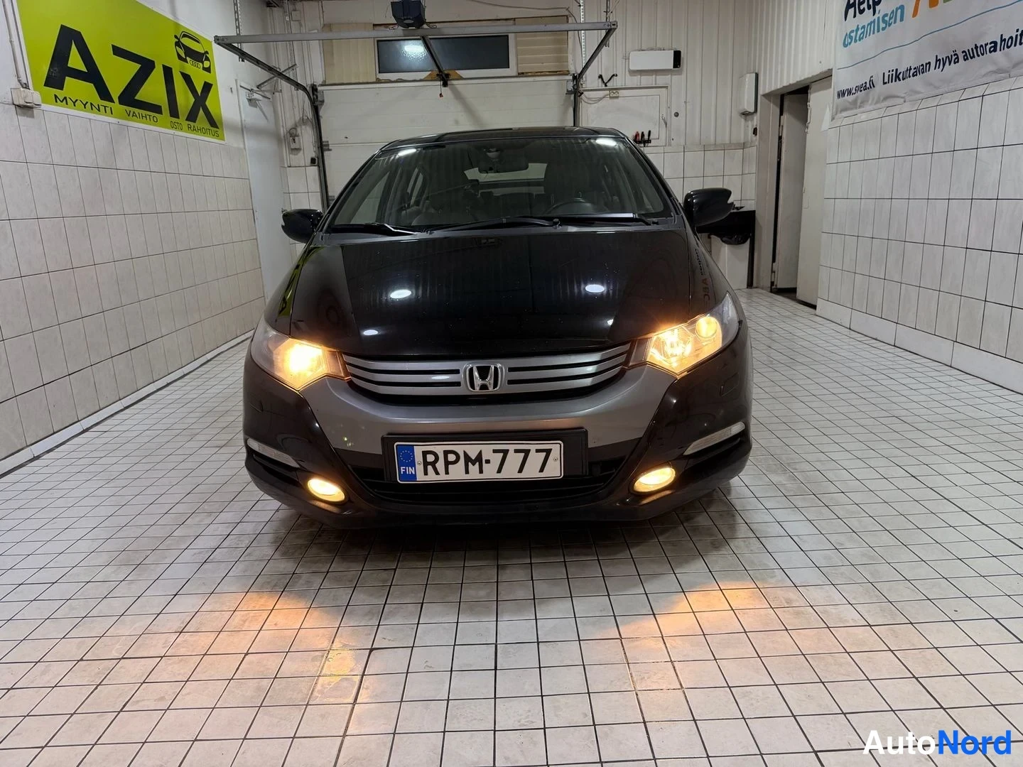 Edestä: Mustan Honda Insightin etupää näkyvissä etuvalot päällä