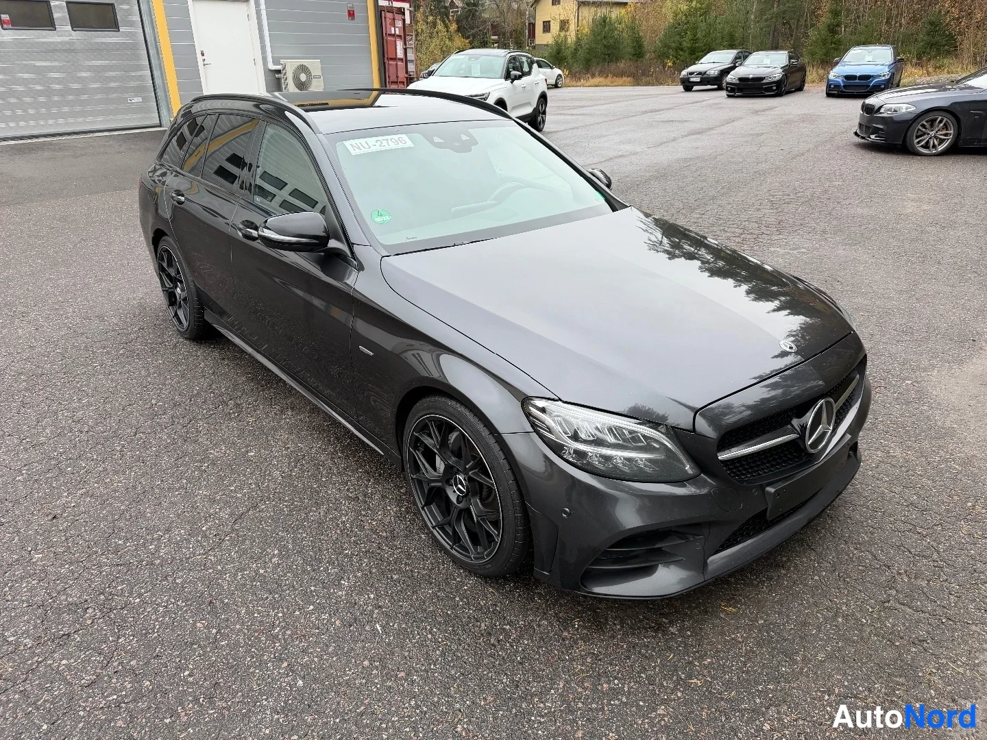 Etuviisto, nokka oikealle: Mercedes-Benz C 220 farmari ylhäältä edestä oikealta kuvattuna, tummanharmaa kori ja mustat vanteet parkkipaikalla.