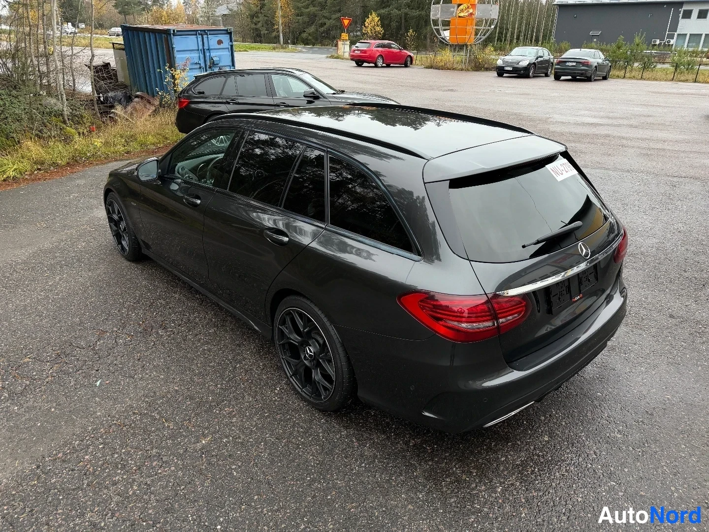 Takaviisto: Mercedes-Benz C-sarjan farmariauto takaa toisesta sivusta kuvattuna, tummanharmaa kori, mustat kevytmetallivanteet, märkä asfaltti.