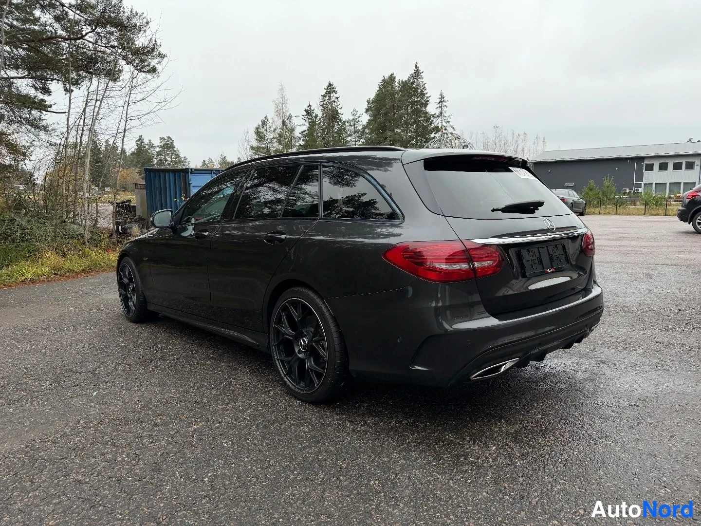 Takaviisto: Mercedes-Benz C-sarjan farmariauto takaa sivulta kuvattuna, tummanharmaa kori, mustat vanteet, kromilista takaluukussa.