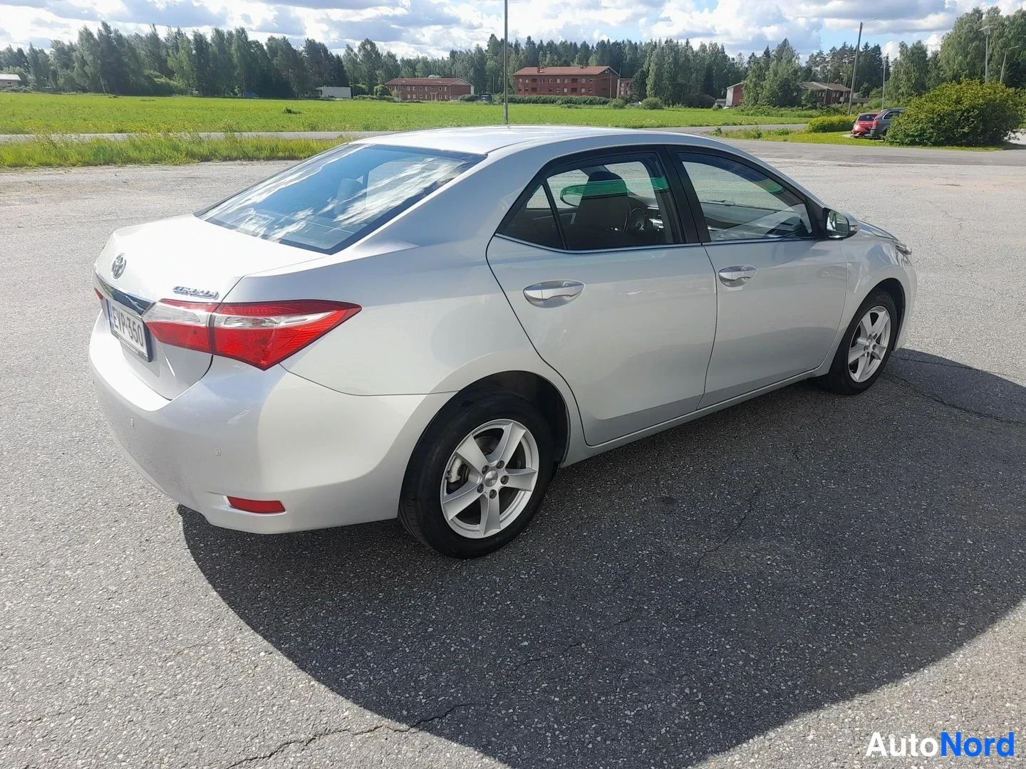 Takaviisto: Toyota Corolla -sedanin takakulmanäkyvys: hopeakorinen auto takaa ja vasemmalta sivulta, rekisterikilpi ja takavalot näkyvät.