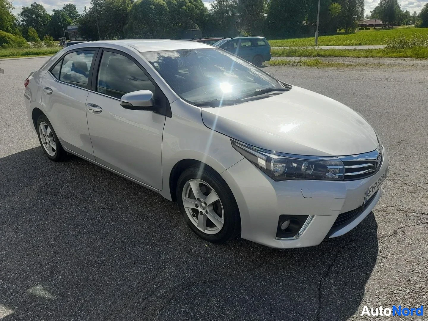 Etuviisto, nokka oikealle: Toyota Corolla -sedanin etukulmanäkyvys vasemmalta: hopea korimalli, keulagrigoriate ja etumoottori näkyvät yhdessä