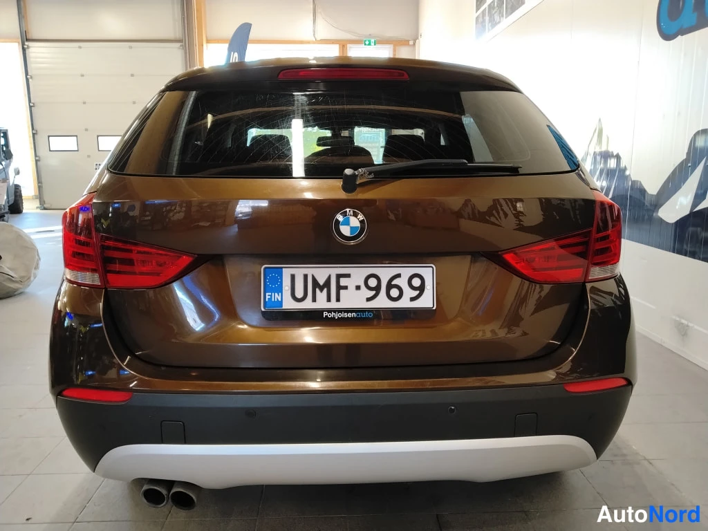 Takaa: Ruskean BMW X1:n takaa otettu yleiskuva, BMW-merkki ja rekisterikilpi.