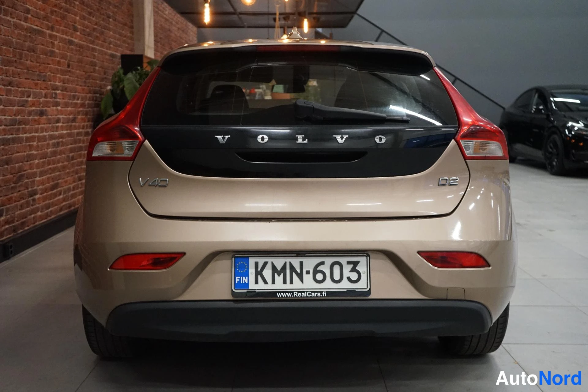 Takaa: Beige Volvo V40 takaa päin, takaovessa V40- ja D2-merkit, rekisterikilpi.