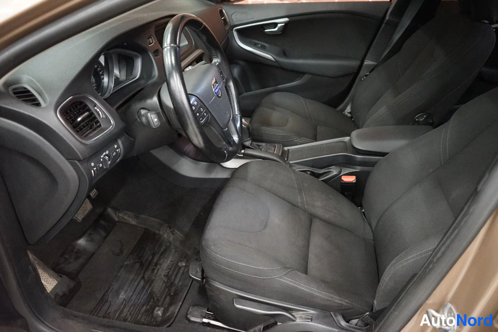 Sivulta: Volvo V40:n ohjaamo vasemmalta: musta tekstiiliverhoilu, Volvon ohjauspyörä ja vaihteenvalitsin.