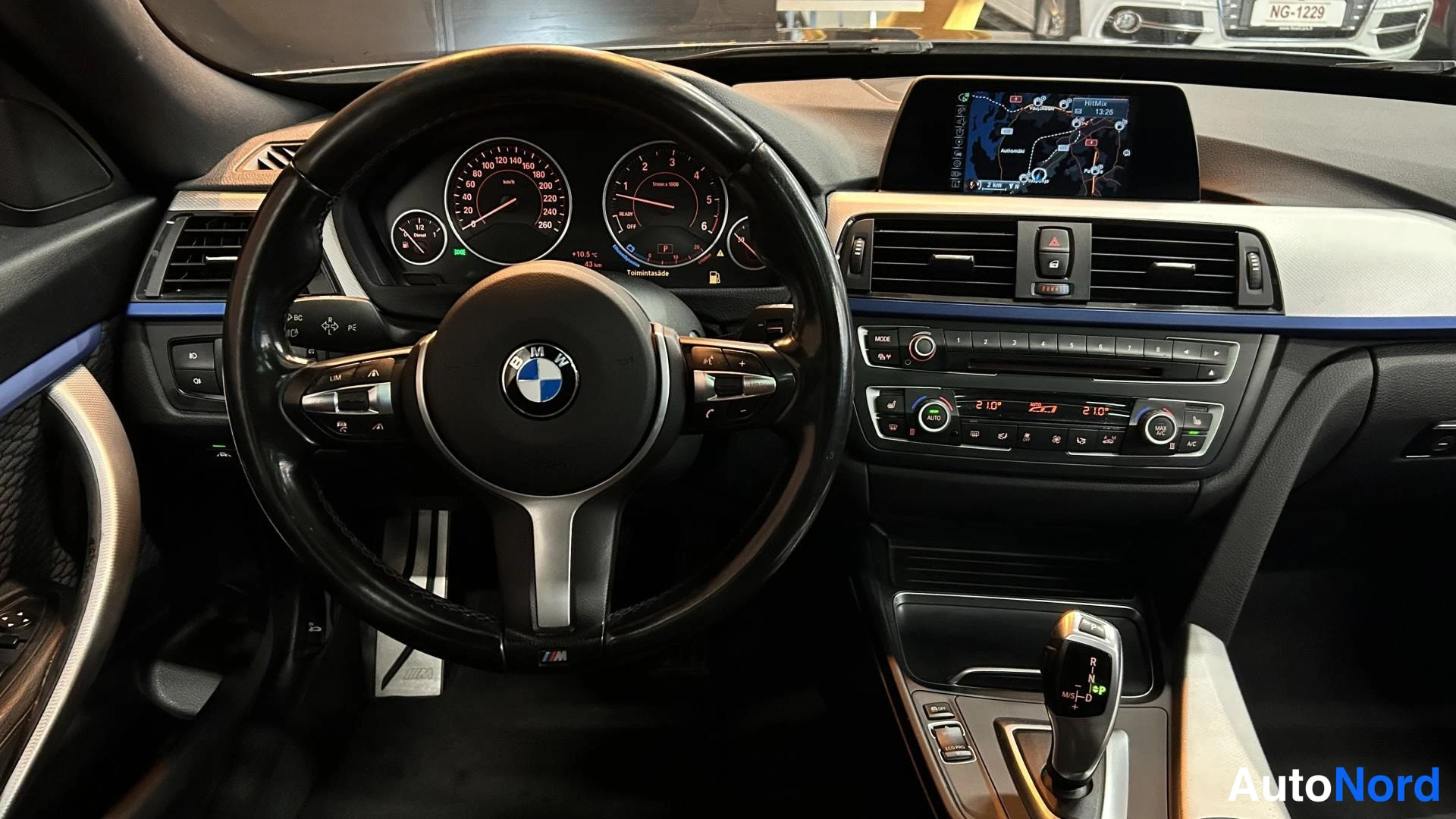 Muu: Kuljettajan näkymä kojelautaan: BMW-ohjauspyörä, analogiset mittarit, keskikonsolin näyttö ja vaihtajan D-tila valittuna.