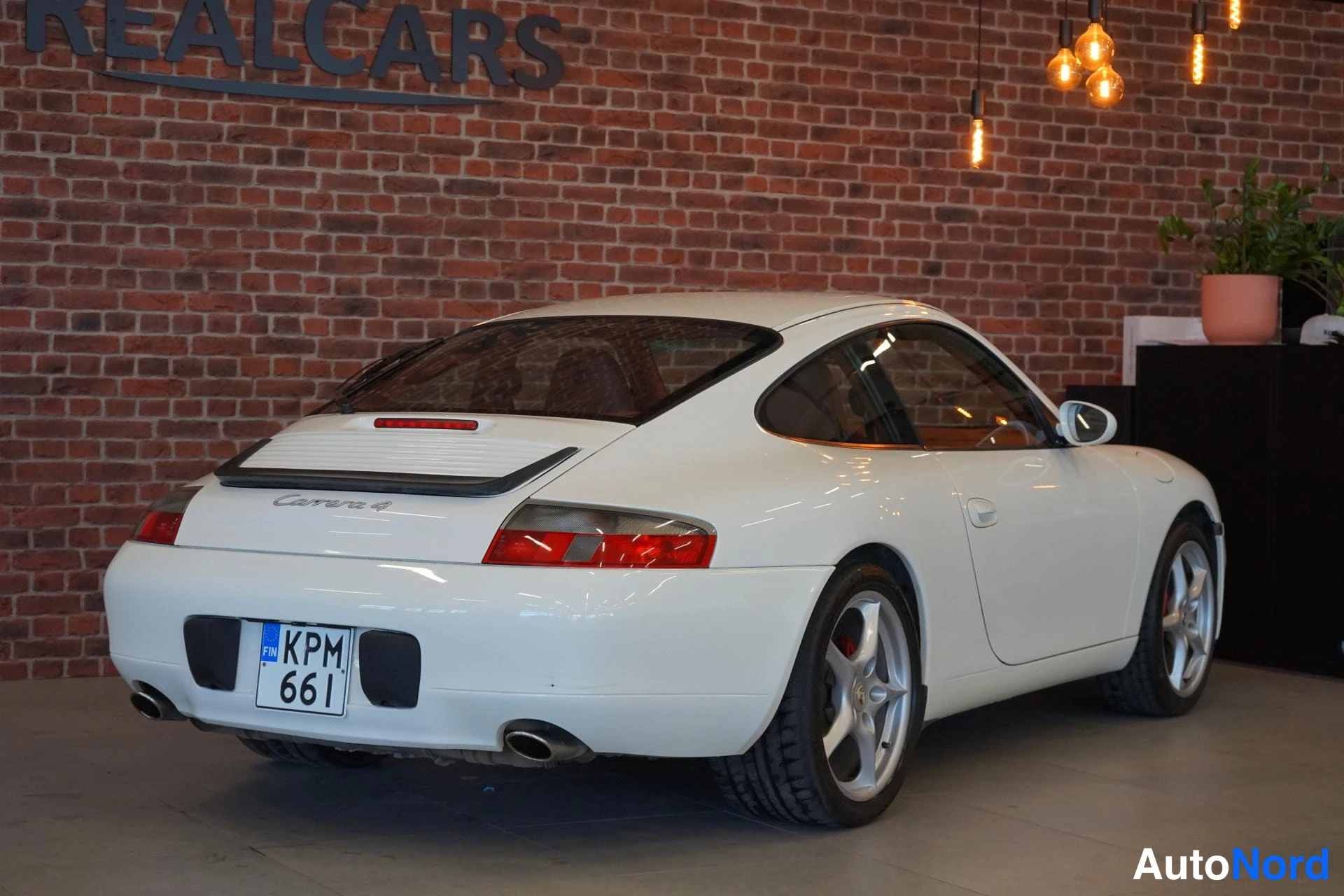 Takaviisto: Valkoisen Porsche 911:n takaosa ja oikea kylki kolme neljäsosasta takaa kuvattuna; takana Carrera 4 -merkintä ja KPM 661 -rekisterikilpi.