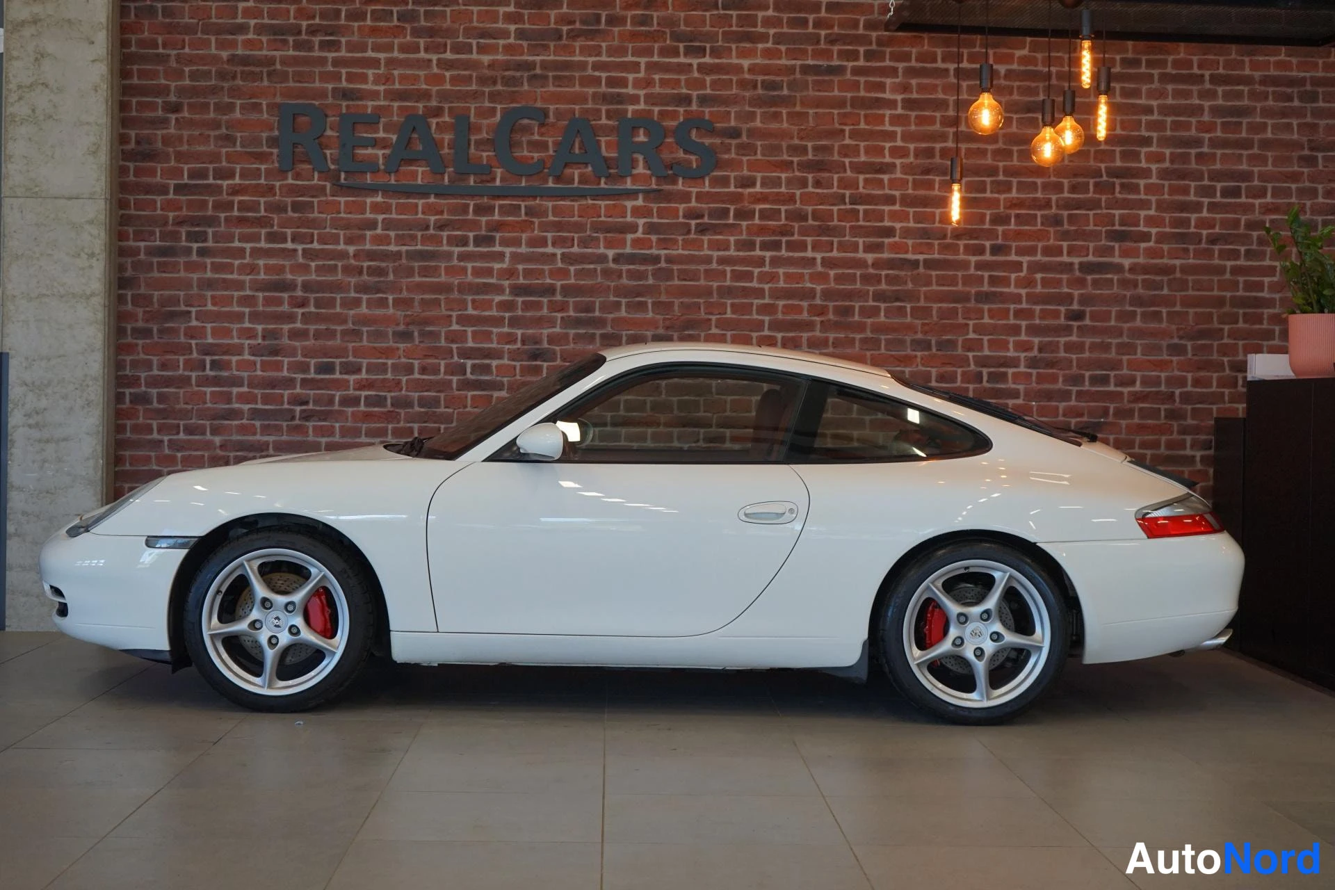 Sivulta: Valkoinen Porsche 911 -urheiluauto sivusta sisätiloissa tiiliseinää vasten.