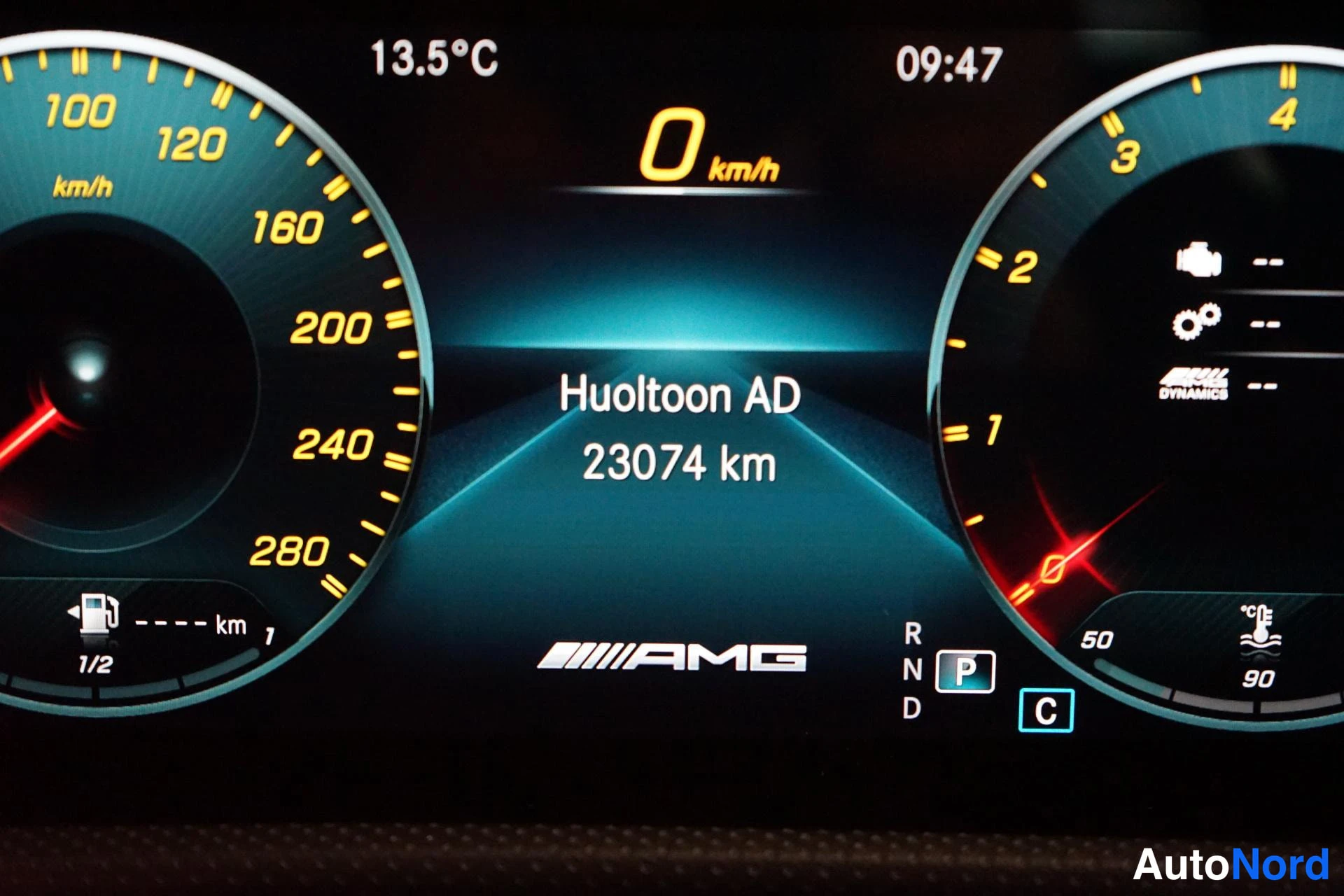 Muu: Mittariston huoltomuistutus 'Huoltoon AD 23074 km', nopeusmittari 0 km/h, lämpötila 13,5°C, vaihde P ja C-napit.