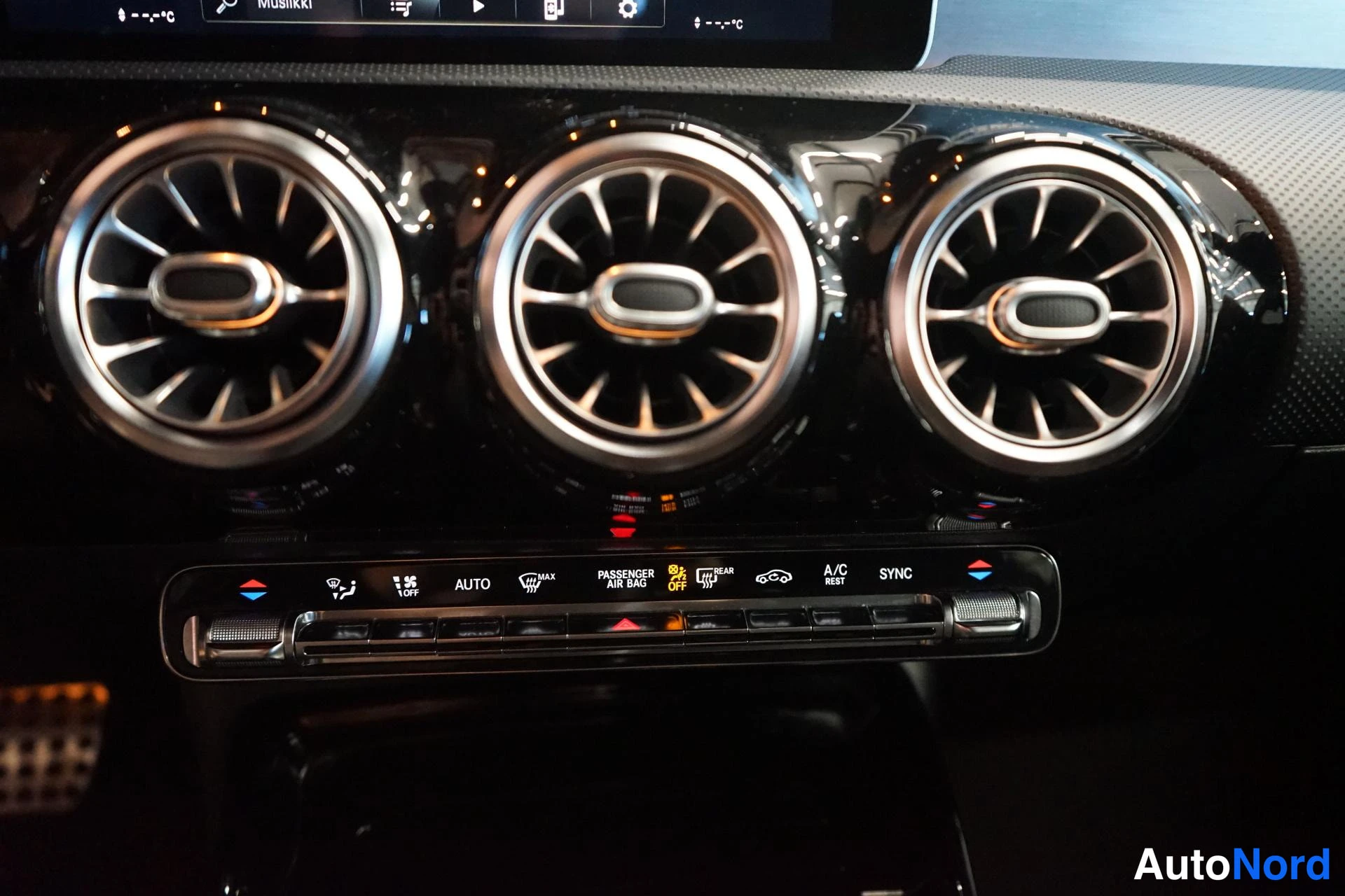 Muu: Auton kojelaudan kolme pyöreää ilmastointisuutinta ja alla oleva lämmityksen ja ilmastoinnin painikepaneeli, jossa lukee mm. AUTO, A/C ja SYNC.