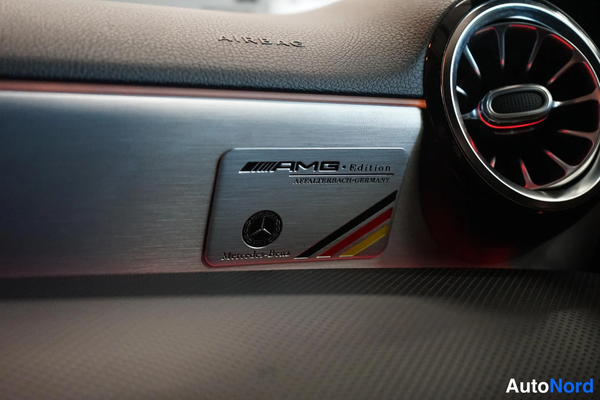 Yksityiskohta: Sisätilan detailikuva: kojelaudan koristeellinen metallikyltti AMG Edition Affalterbach-Germany Mercedes-Benz -tekstillä, oikealla pyöreä ilmastointisuutin.