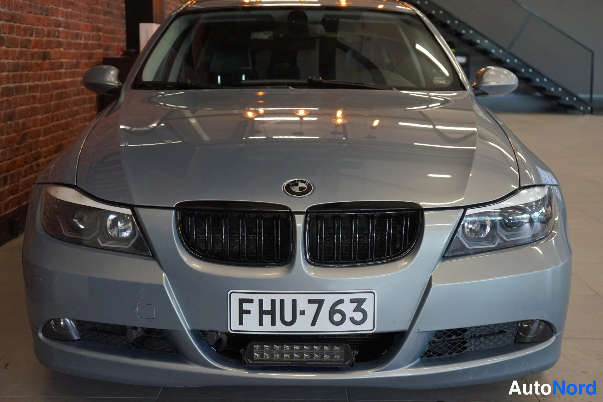 Edestä: Hopeanharmaa BMW-porssin edessäpäin, etusäleikkö ja molemmat ajovalot näkyvät, rekisteri.