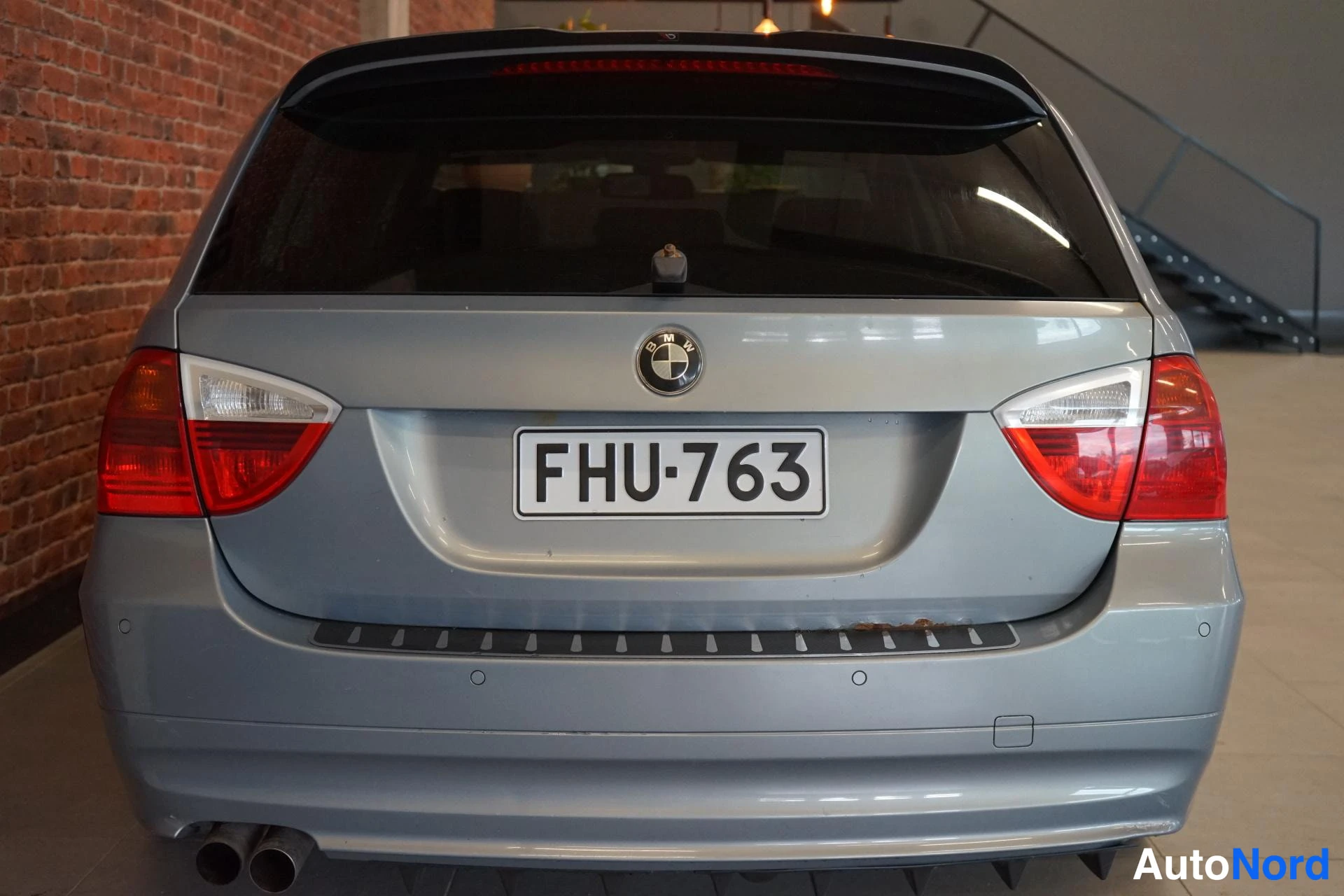 Takaa: Hopeanharmaa BMW:n takaosa suoraan takaa, takavalojen ja takaluukun rekisteri, kaksoispakoputki näkyy alhaalla.