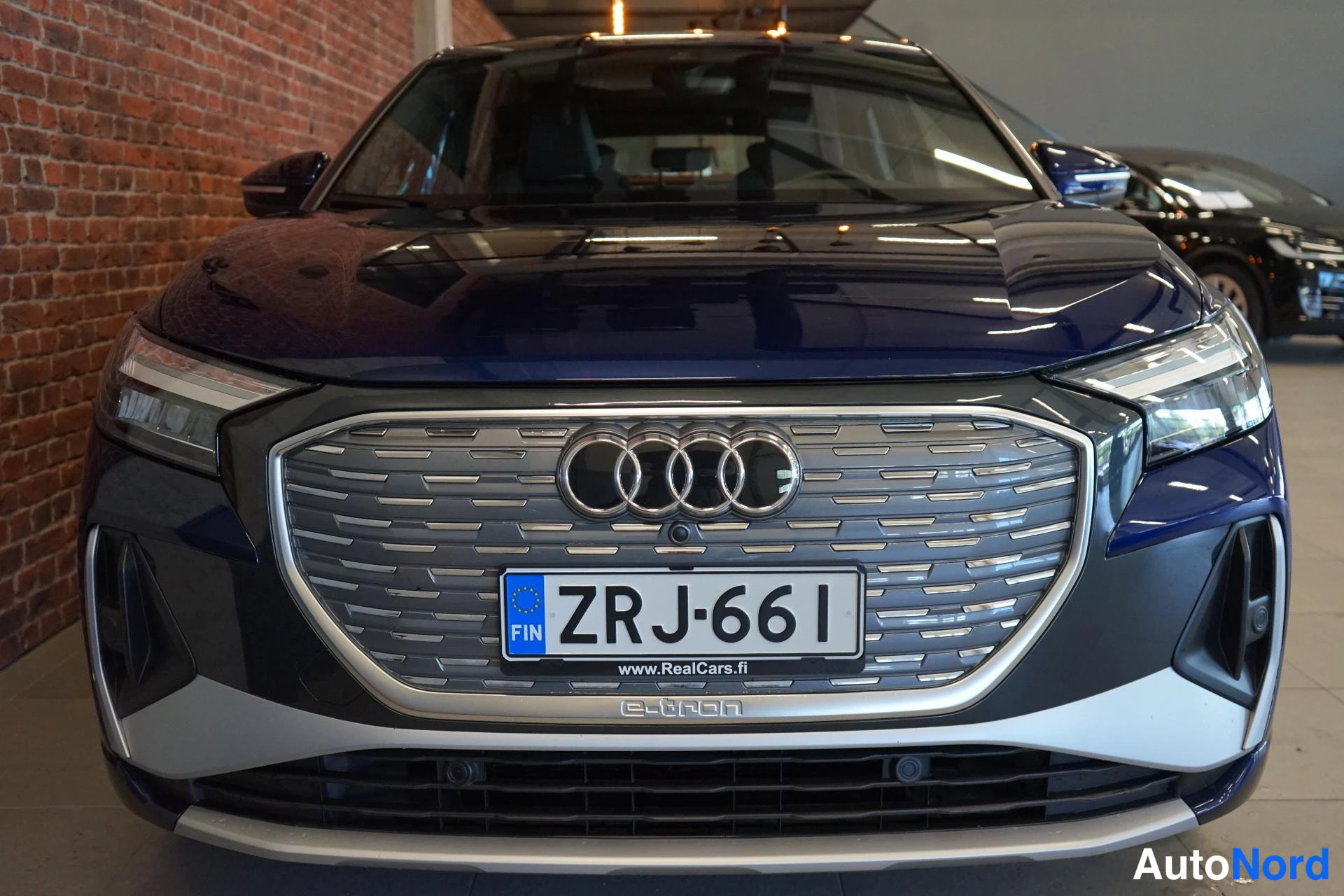 Edestä: Edestä kuvattu tummansininen Audi, keulassa Audi-neljä renasta -tunnus, rekisteritunnus ja e-tron-teksti etupuskurissa.