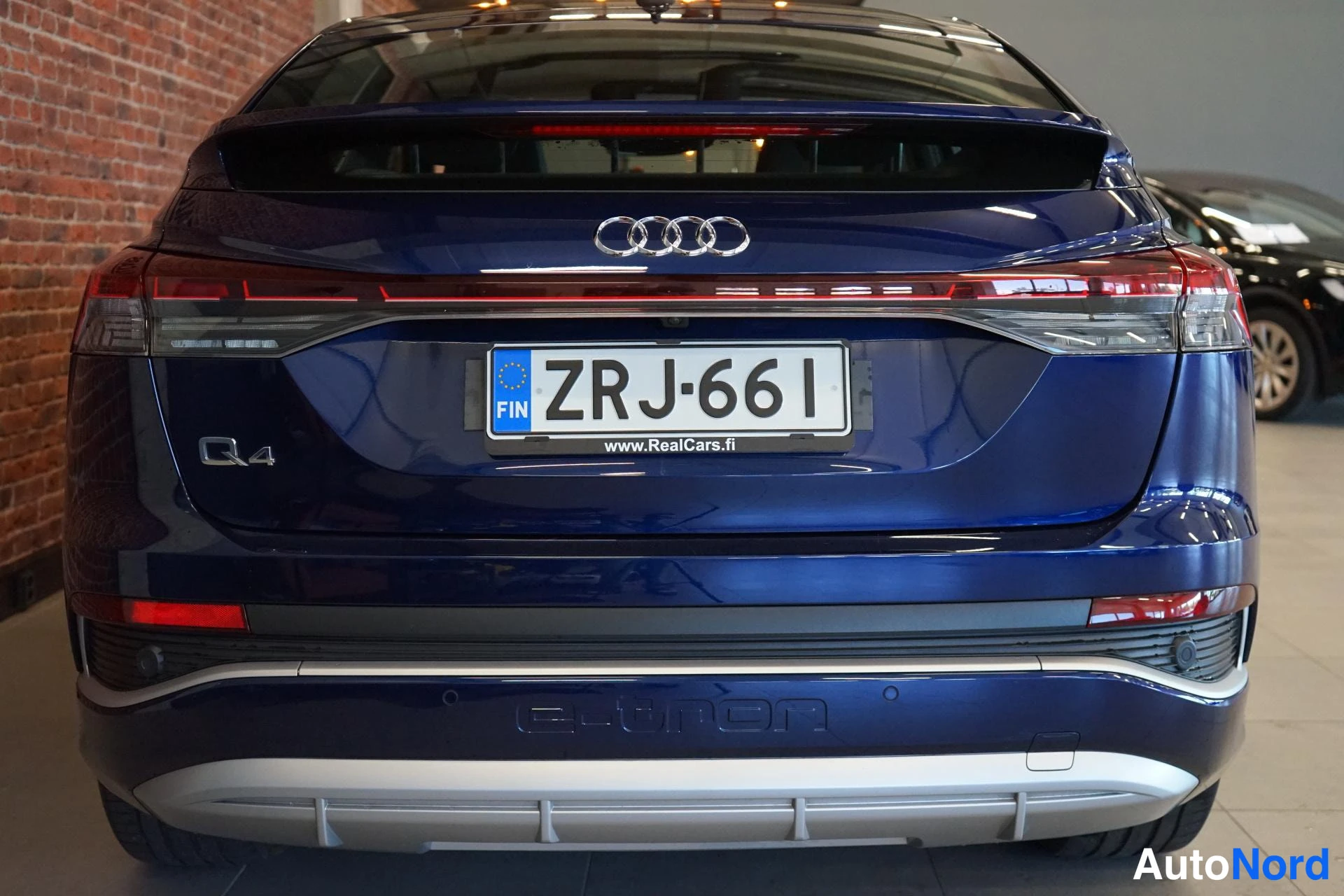Takaa: Takaapäin kuvattu tummansininen Audi Q4 e-tron, rekisteritunnus, Q4-merkintä takaluukussa ja poikittainen takavaloryhmä.