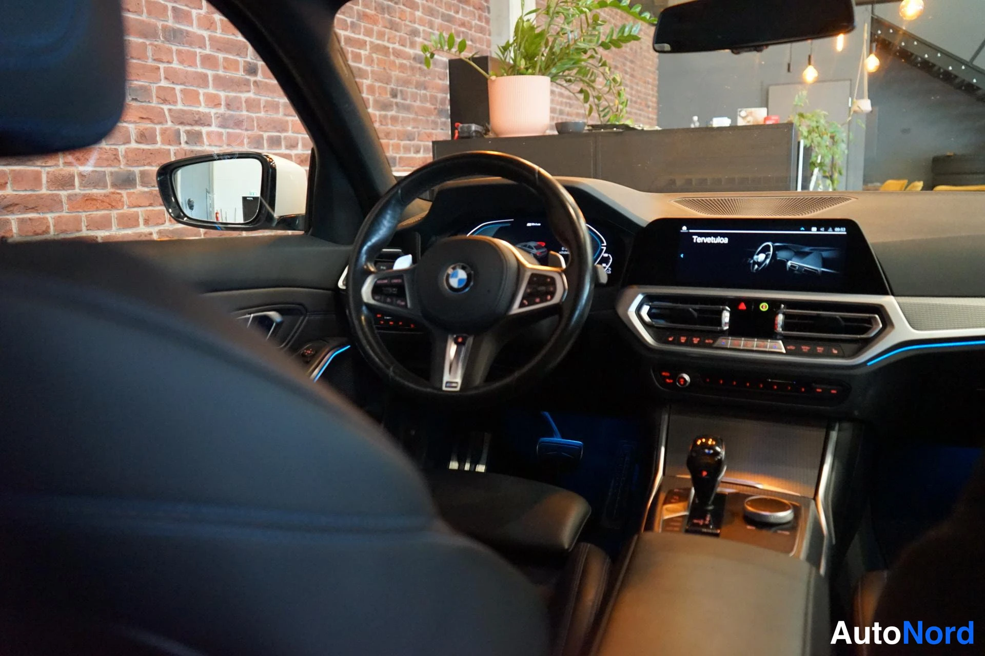 Edestä: Auton sisätilat: BMW-ohjauspyörä, digitaalinen mittaristo ja kosketusnäyttö, jossa lukee Tervetuloa.