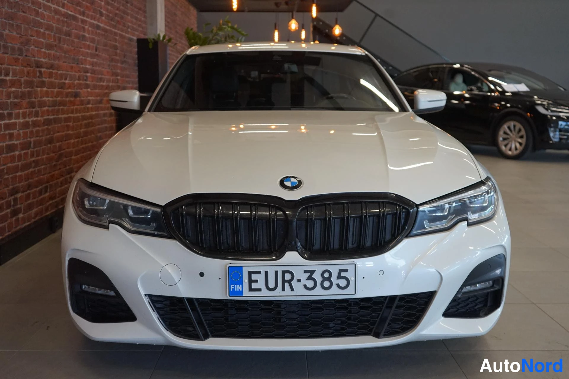 Edestä: Valkoisen BMW:n keula suoraan edestä, musta munuaissäteilujen, LED-etuvalot ja rekisterikilpi.