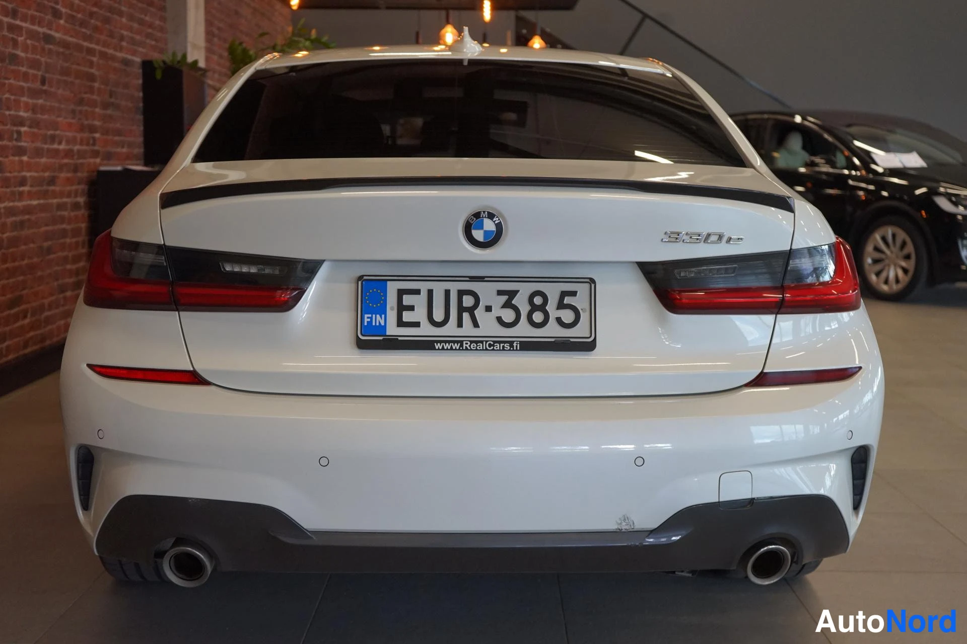 Takaa: Valkoisen BMW:n perä suoraan takaa, 330e-merkintä, punaiset takavalot, kaksosputkisto ja rekisterikilpi.