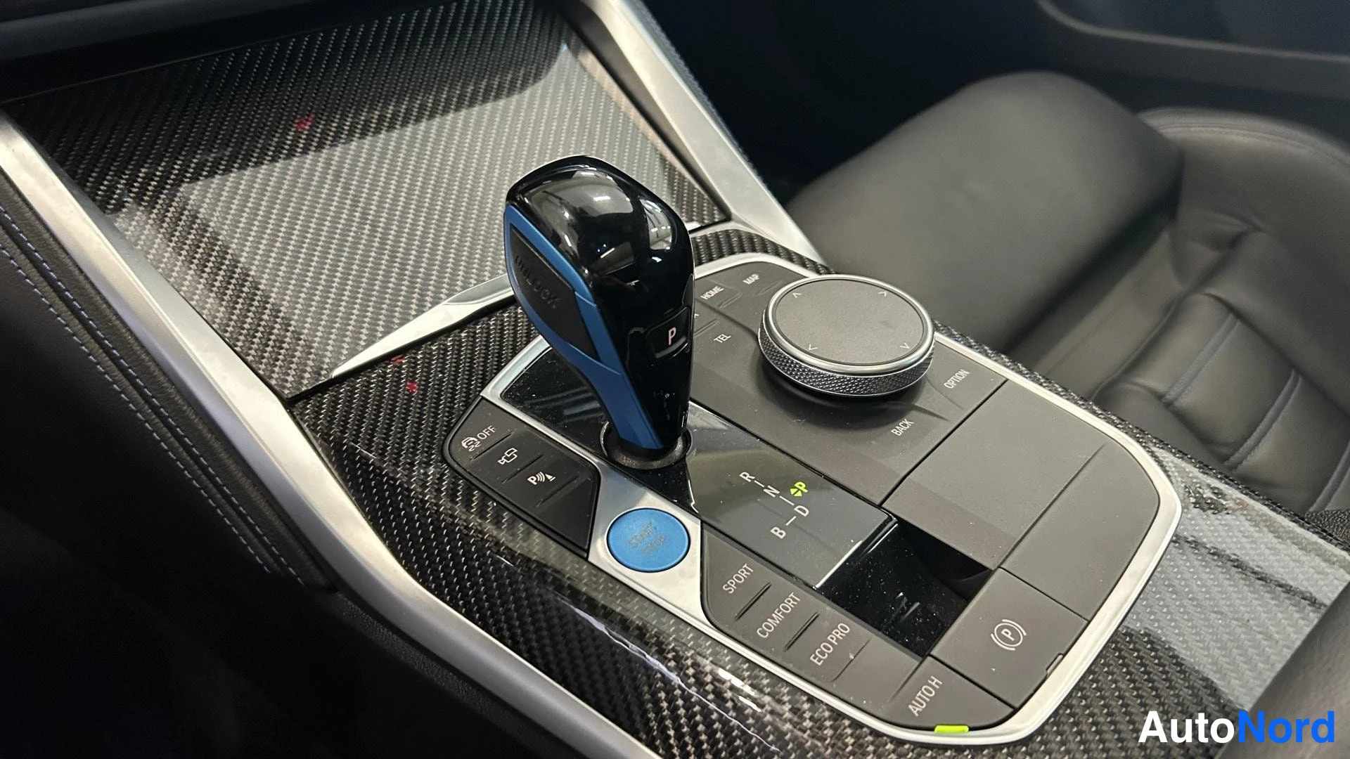 Muu: Auton keskikonsoli: vaihdevipu, iDrive-ohjainkärry ja ajovalintanapit (SPORT, COMFORT, ECO PRO) hiilikuvioisella pinnalla.