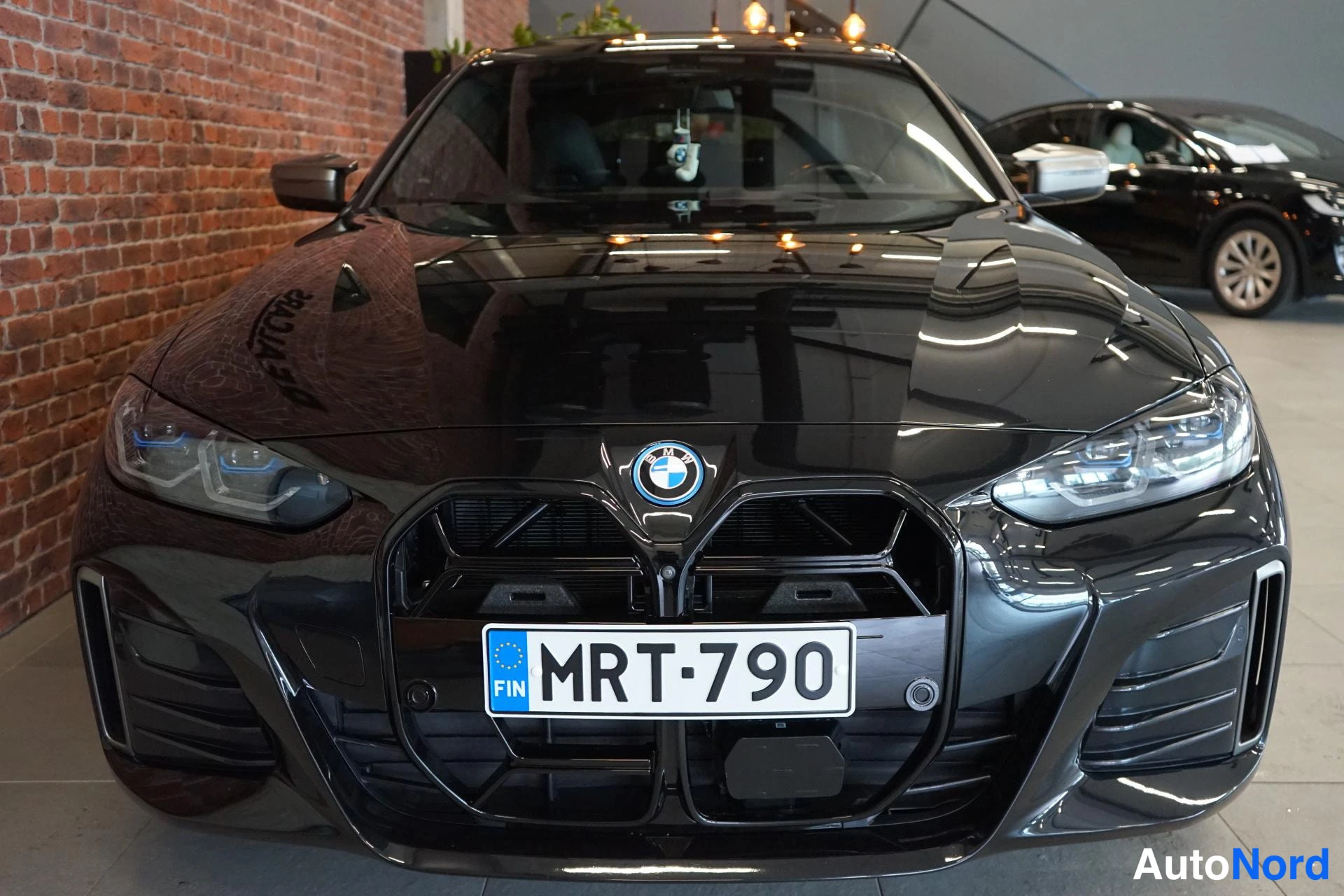 Edestä: Mustan auton etupäätys suoraan edestä, sininen BMW-embleemi ja rekisteritunnus.