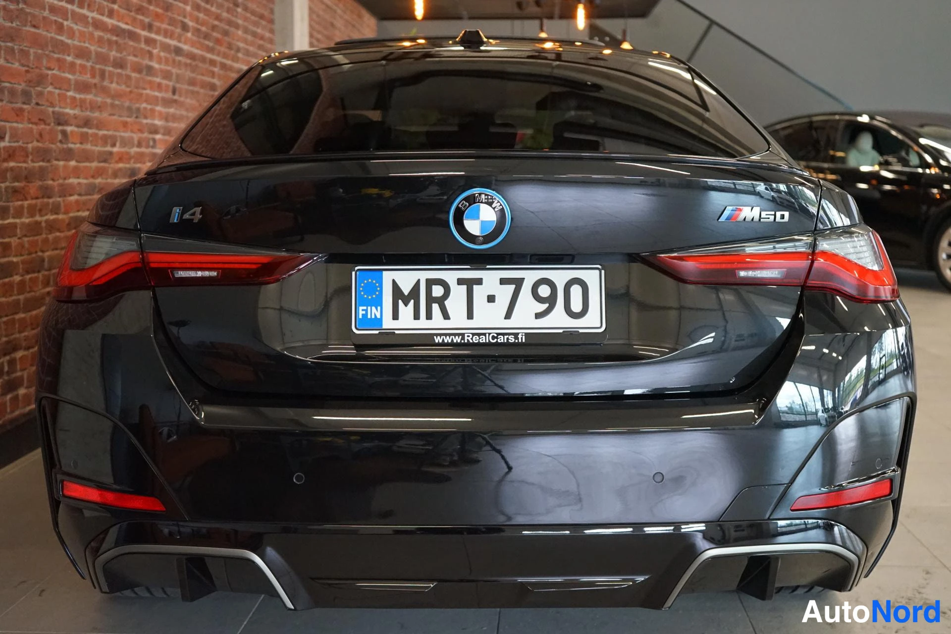 Takaa: Mustan auton takapäätys suoraan takaa, i4 ja M50 -merkinnät, rekisteritunnus.