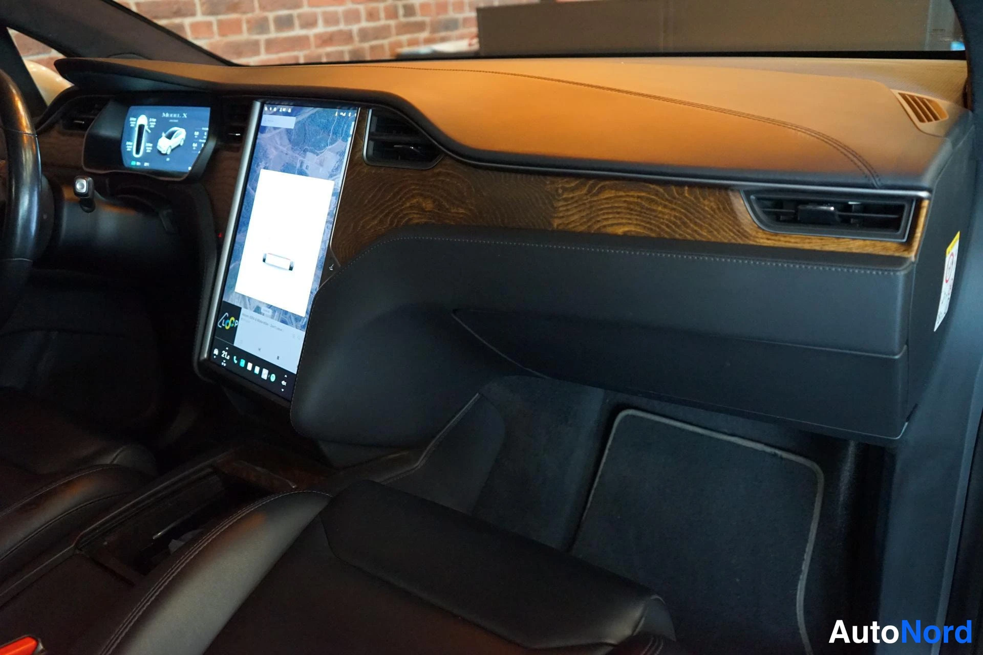 Etuviisto, nokka vasemmalle: Tesla Model X:n kojelaudan tarrat ja suuri keskikosketusnäyttö, puupinta ja ilmastointilaitteet näkyvät.