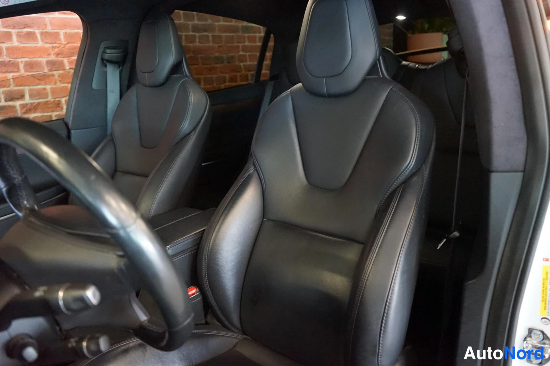 Muu: Tesla Model X:n etumatkustustila: kaksi mustaa nahkapenkin istuinta ja ohjauspyörän reuna näkyvät; avoimella takapenkkialueella.