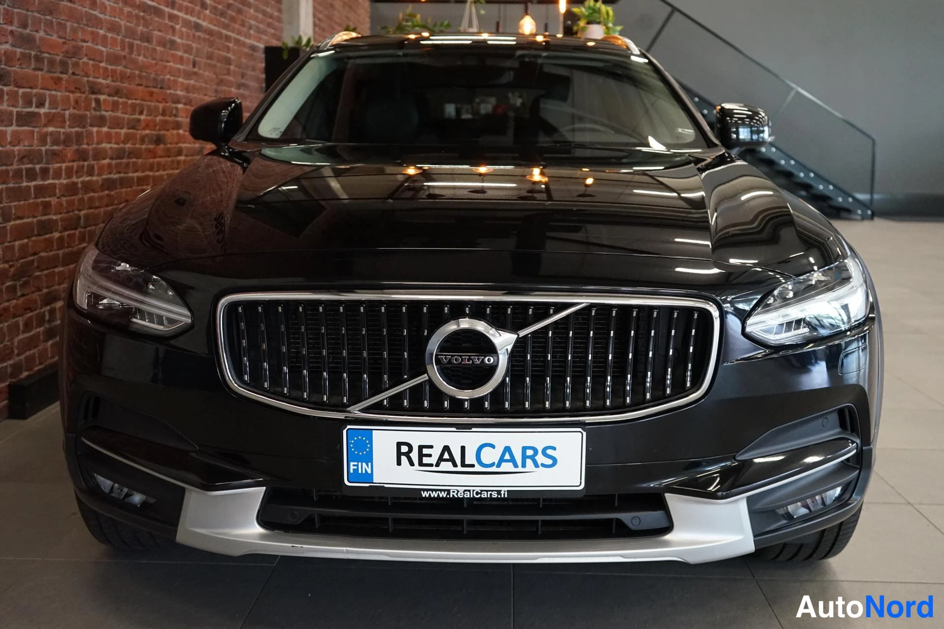 Edestä: Mustan Volvon keula edestä, kyltti REALCARS etupuskurissa.