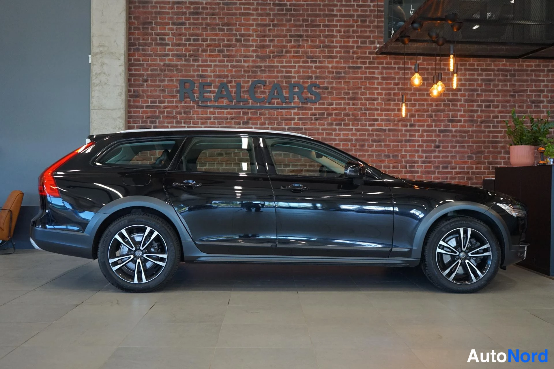 Etuviisto, nokka oikealle: Mustan V90 Cross Country -farmarin kylkikuva, jossa näkyvät vasemman puolen ovet, hieman etusarvikkasta ja rekisteritunnuksellinen etuosa.