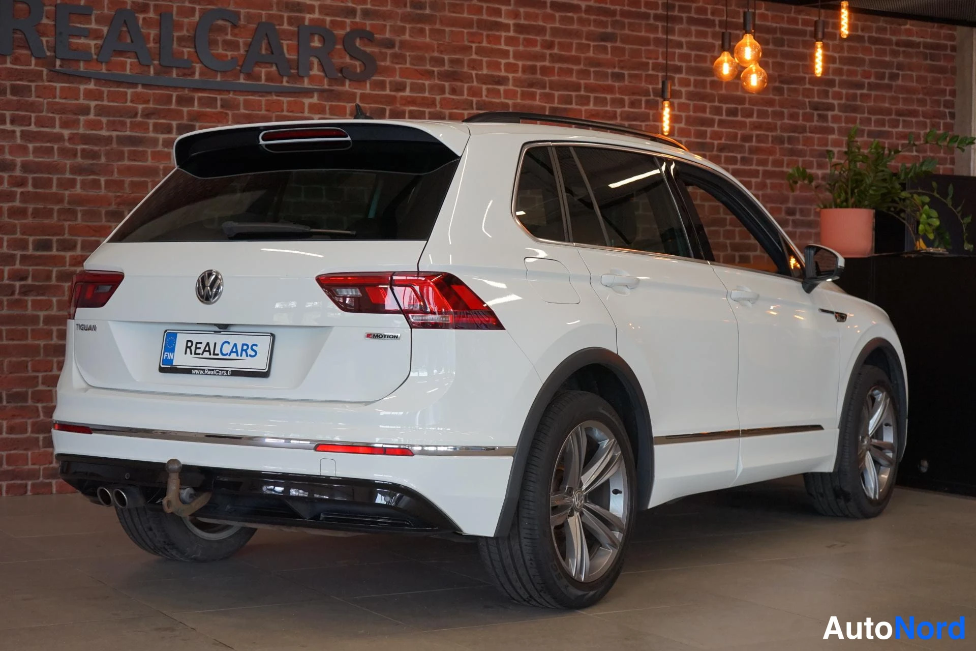 Takaviisto: Valkoisen tila-autojen takakolmannes: takavalot, VW-merkki, kattokaiteet ja vetokoukku näkyvät.