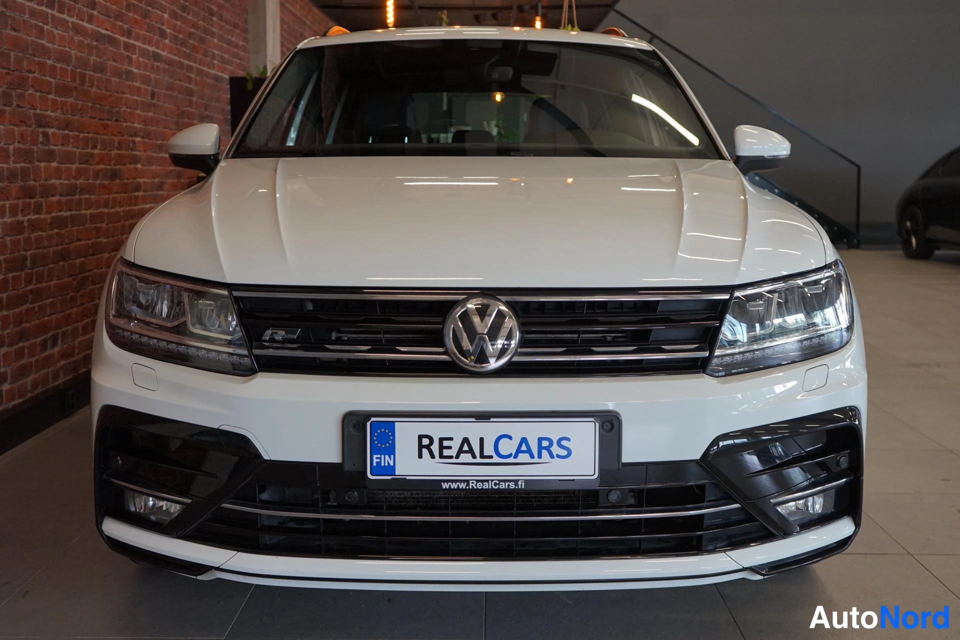 Edestä: Valkoisen tila-auton suora etunäkymä: VW-merkki, etuvalot ja REALCARS-kyltti etupuskurissa.