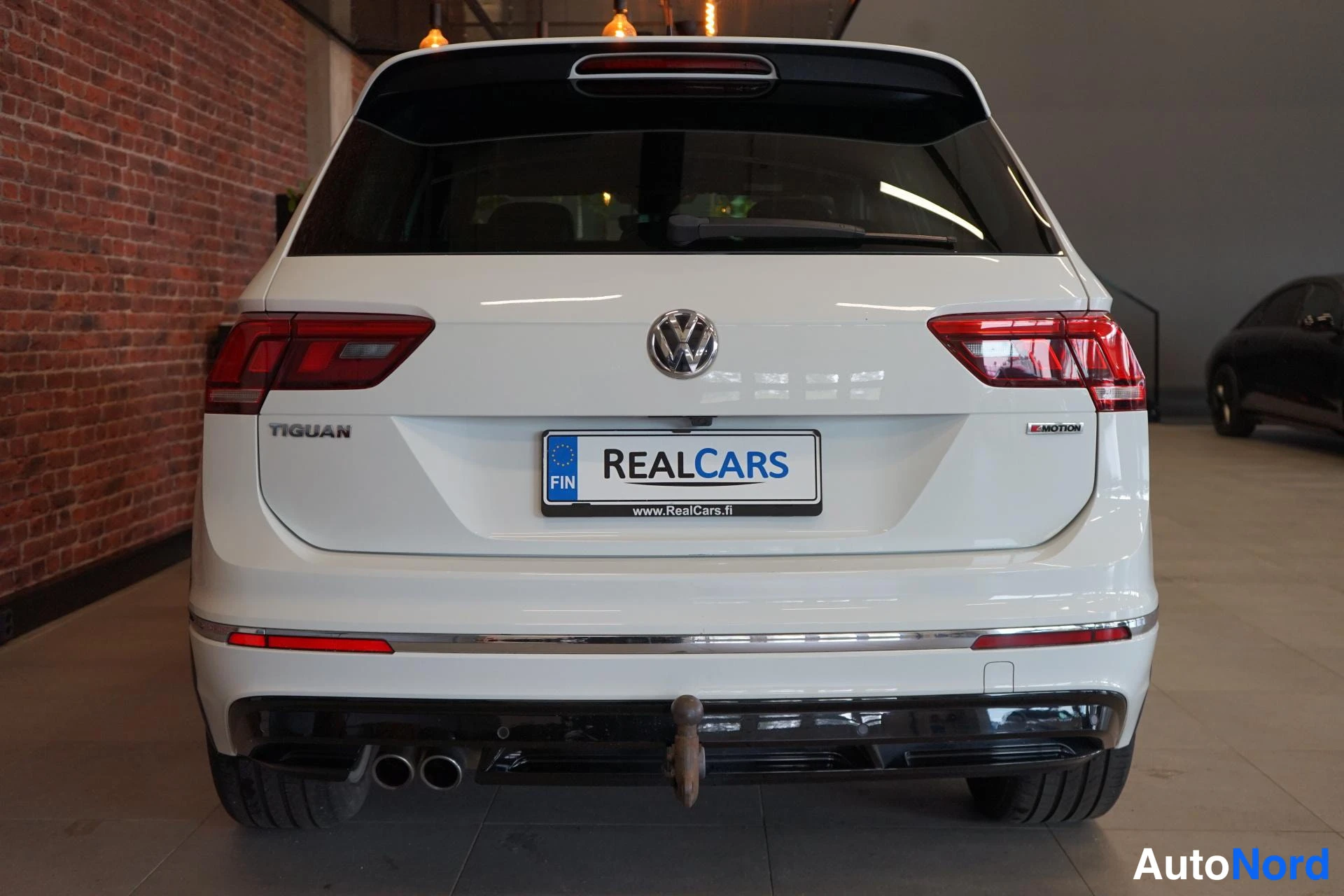 Takaa: Valkoinen Volkswagen Tiguan takaa kuvattuna, takavalot ja TIGUAN-merkintä näkyvissä, koukku takapuskurissa.