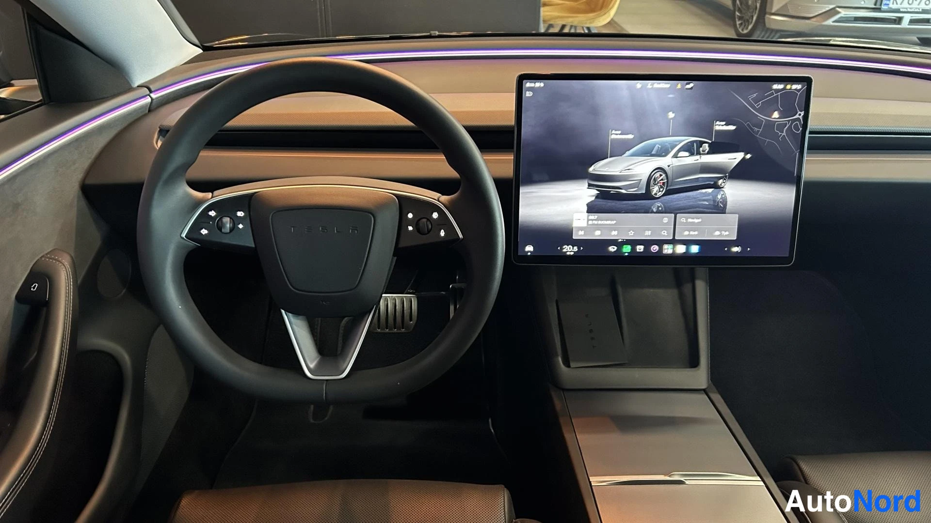 Muu: Kuljettajan puolen sisätila: ohjauspyörä, jossa TESLA-logo, ja suuri keskinäyttö, jonka ruudulla ajoneuvon kuva ja asetusvalikko. Tunnelavavalo kojelaudassa.