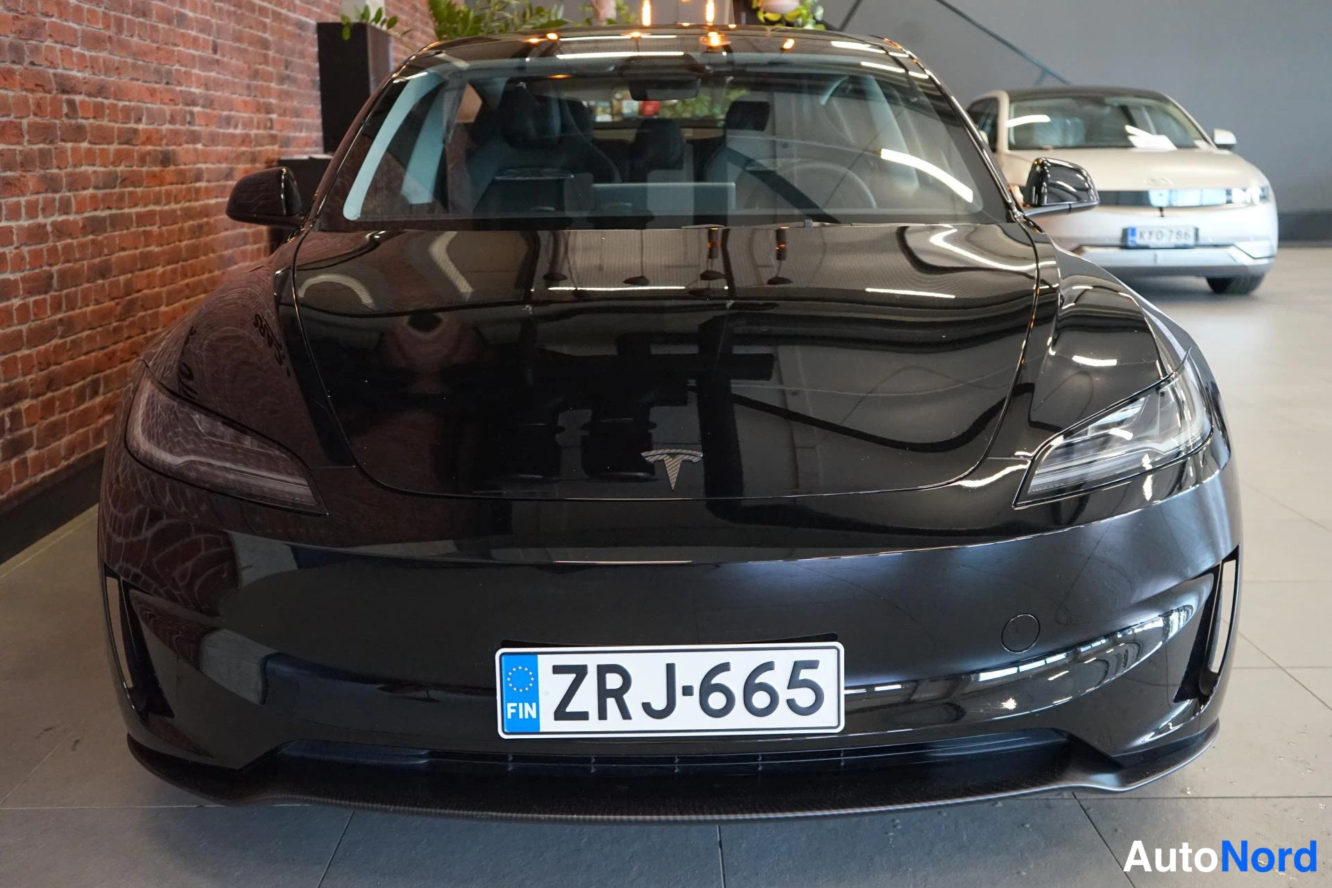 Edestä: Musta Tesla Model 3 edestä päin, rekisterikilpi.