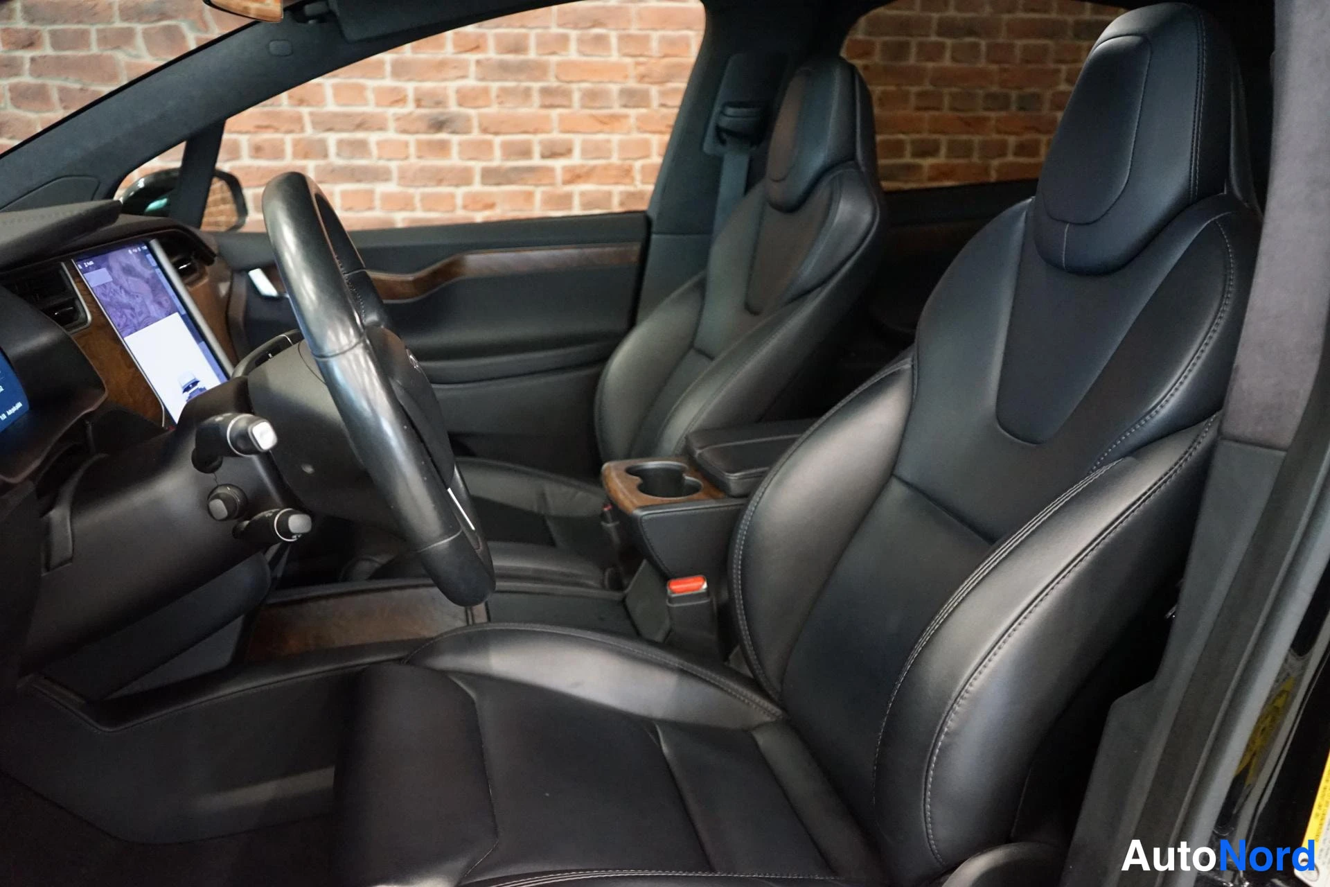 Edestä: Tesla Model X:n sisätilat: ohjauspyörä, keskikonsoli ja kaksi mustaa nahkaistuinta.
