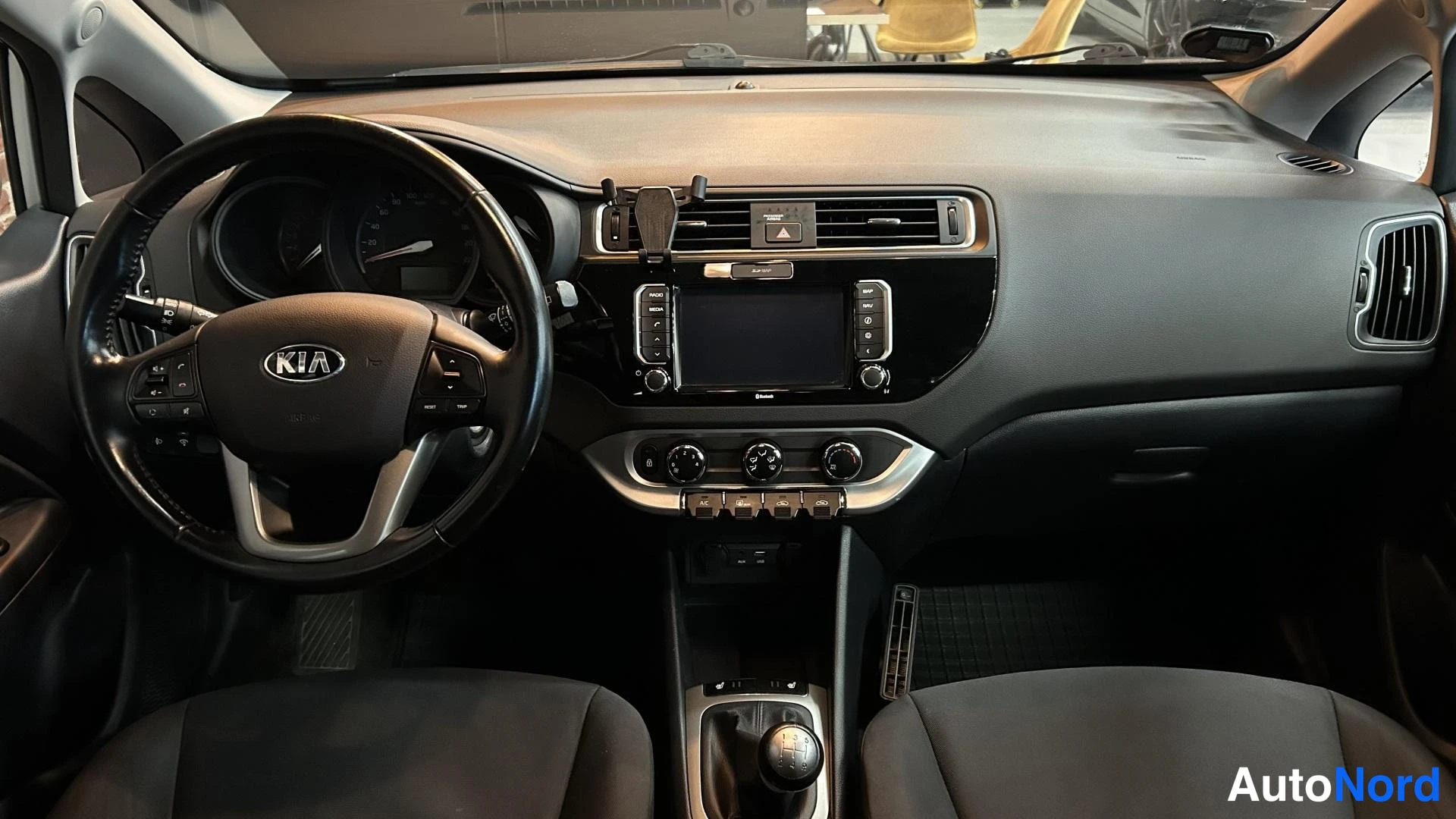 Muu: Auton ohjaamo ylhäältä: KIA-ohjauspyörä, kojelaudan infotainment-näyttö ja keskikonsolin vaihtajanuppivaihde.