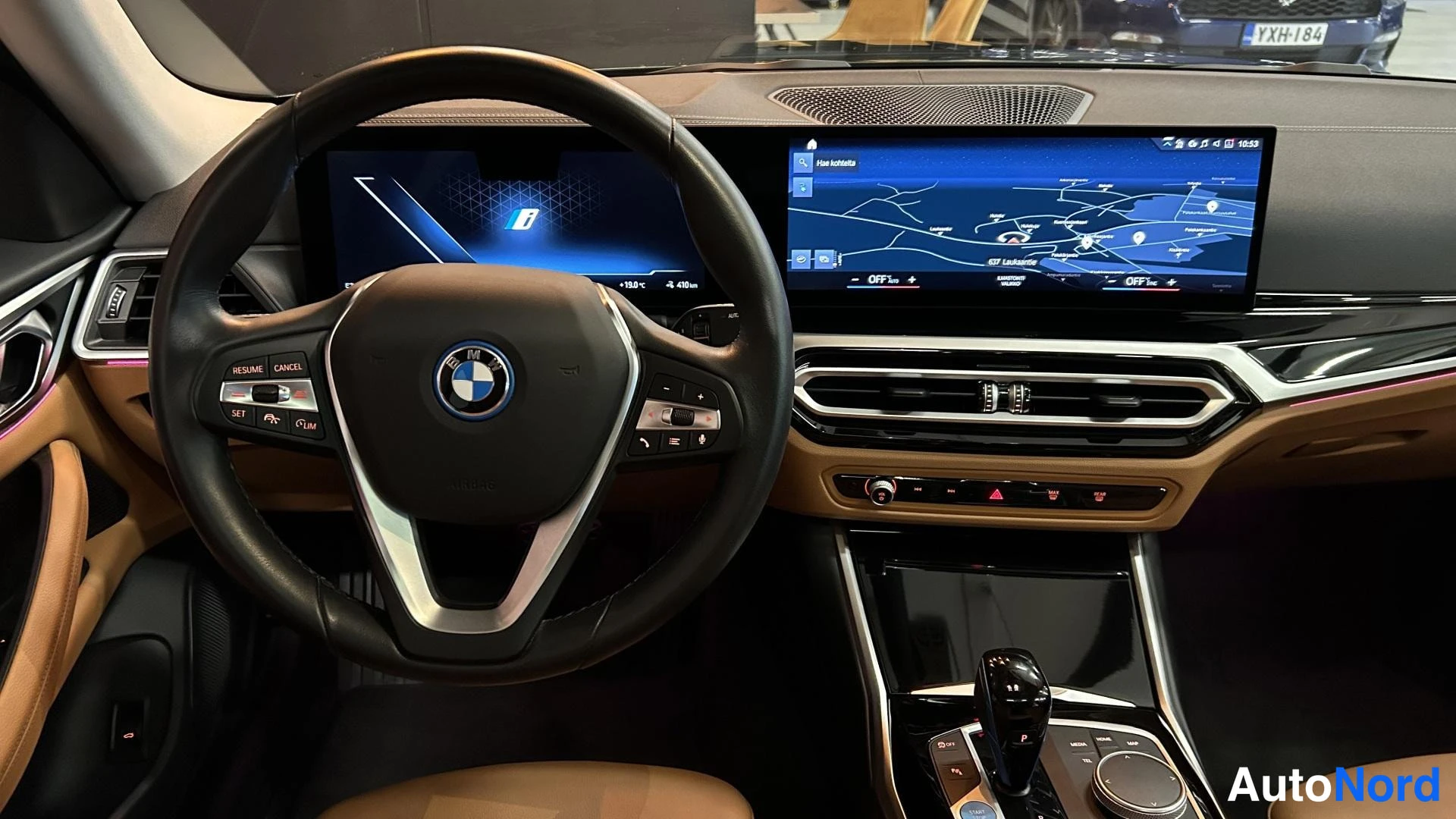 Muu: Lähikuva ohjaamosta: BMW:n ohjauspyörä ja yhdistetty näyttöpalkki kartanäytöllä, vaihteenvalitsin ja ohjaimet.