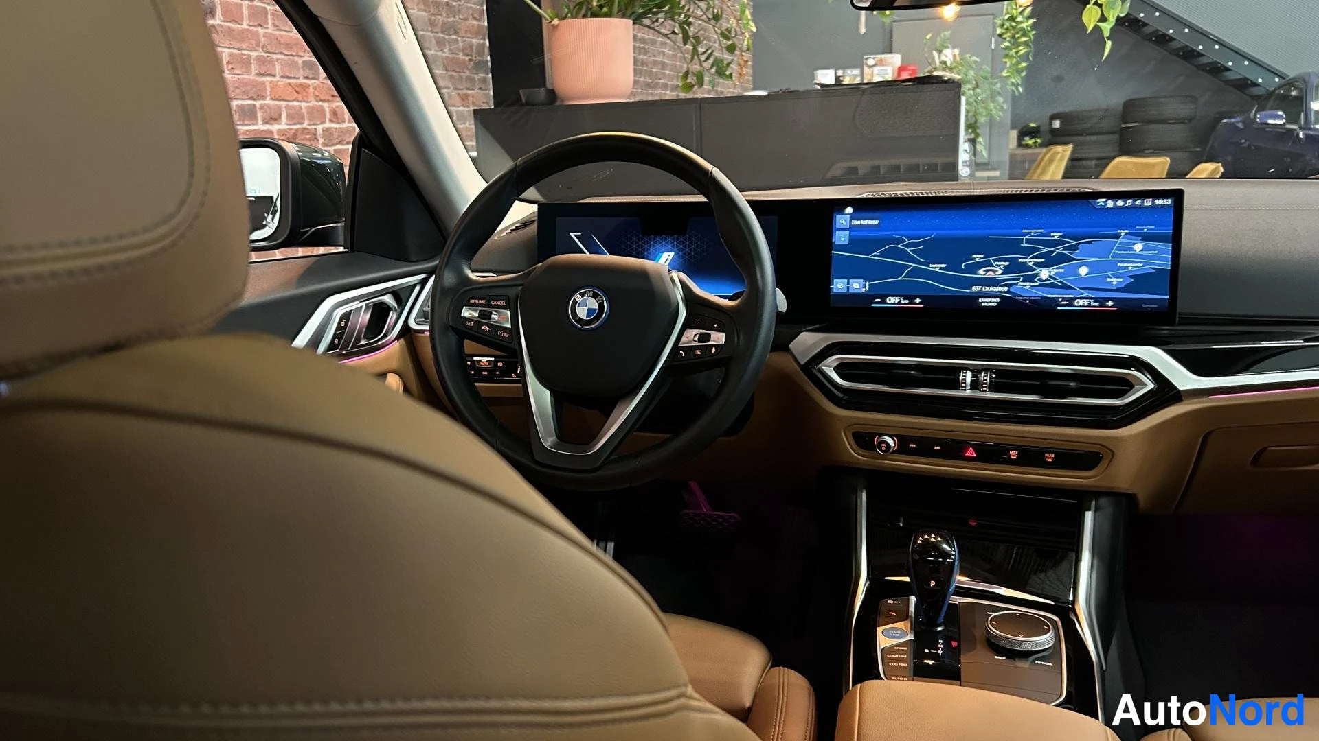 Muu: Auton sisätila: BMW-ohjauspyörä, ruskeat nahkaistuimet ja laaja kaareva näyttö, jolla on kartta.